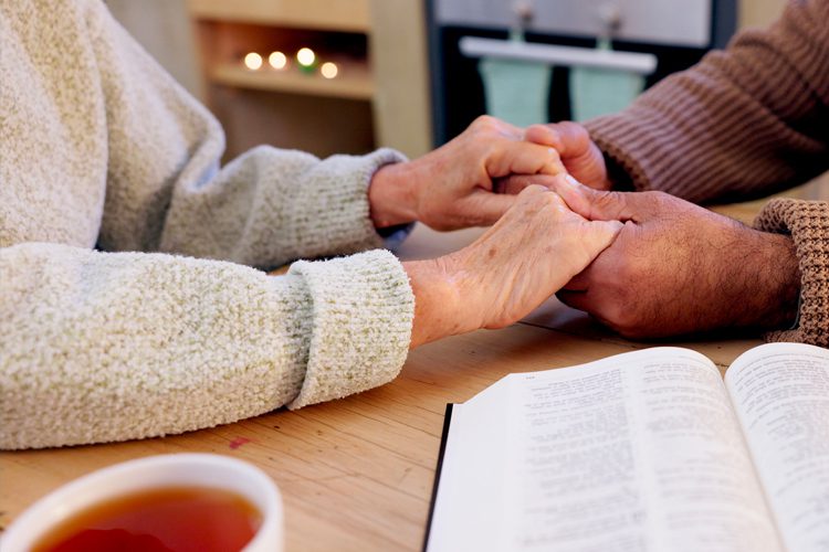 close up of holding hands with bible and cup of tea