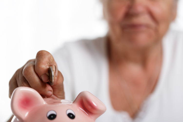 senior woman putting coin into piggy bank